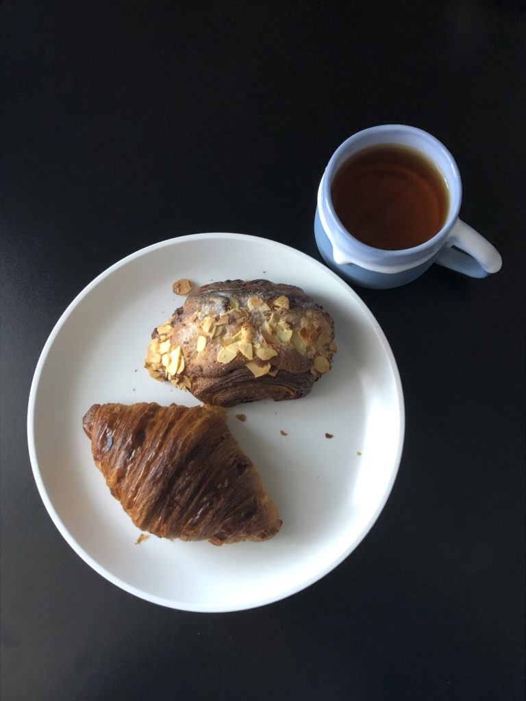白い皿にクロワッサンとチョコダマンドクロワッサン、水色のマグカップに紅茶が入っている。