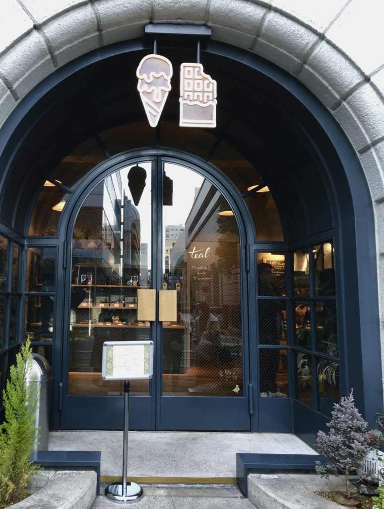 teal玄関。アーチ状の玄関ポーチの天井に、アイスとチョコレートの看板が吊り下がっている。