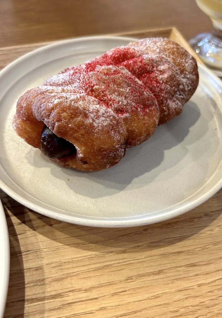 チョコクリームが中に入ったコロネ（ドーナツ）。纏った粉砂糖の上にフランポワーズのパウダーがかかっている。