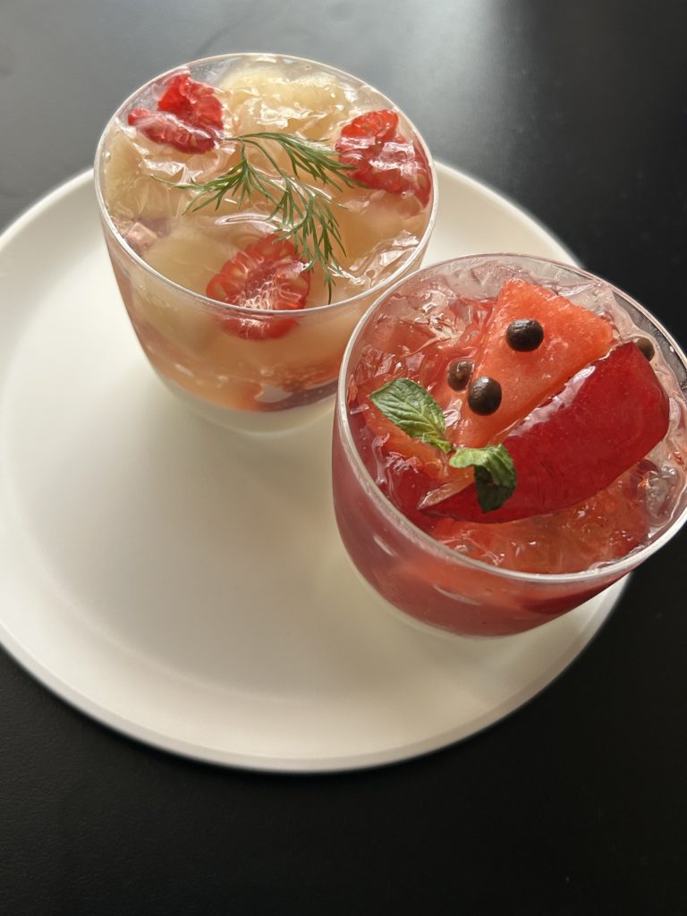 季節のブラマンジェ。サイコロカットした洋梨と半分に切られたラズベリーが薄黄色のジュレに入った洋梨（上）と、薄桃色のジュレから三角カットのスイカとすももが覗き、上からチョコパフが添えられたスイカとすもも（下）。