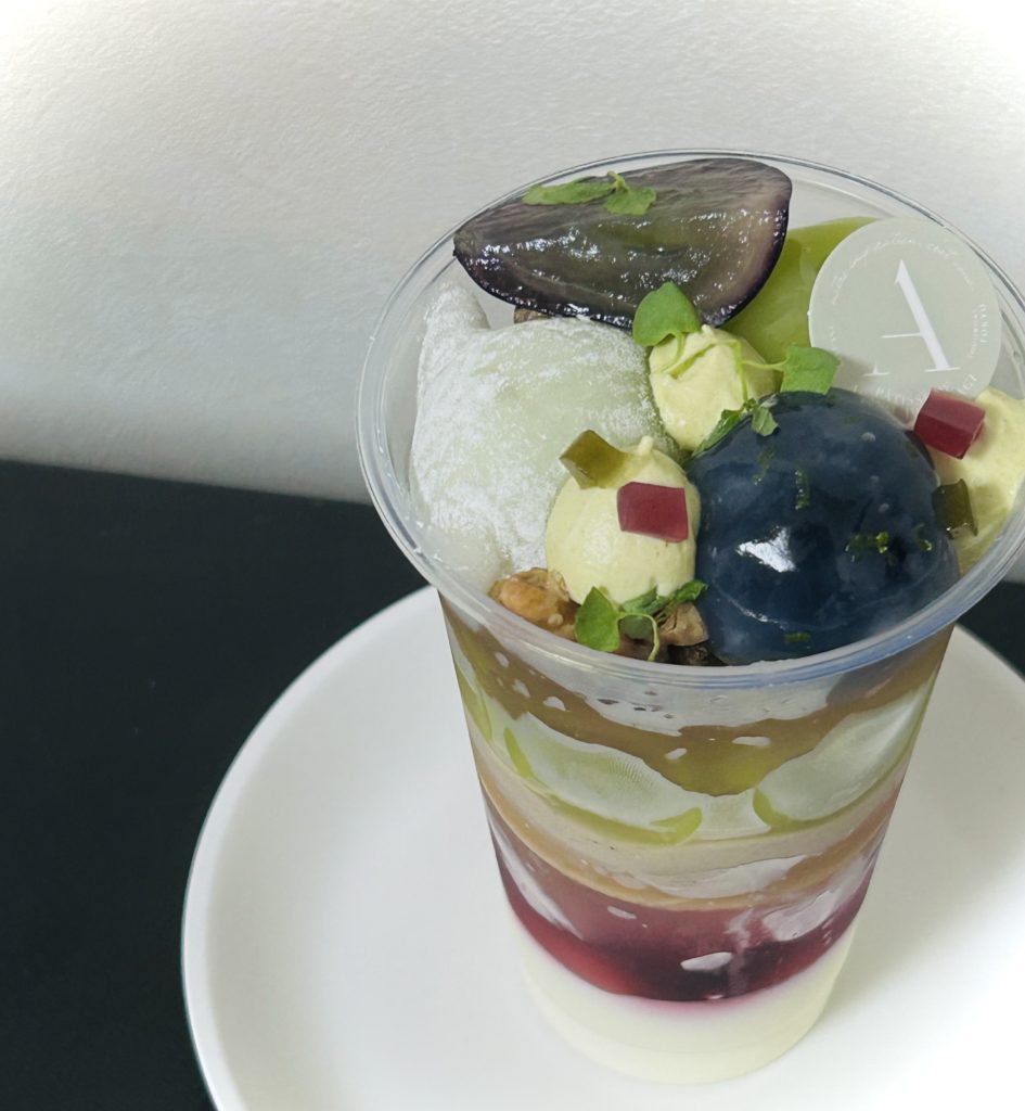 パルフェア アンポルテビジュー レザン（上）
透明な薄い葛のような膜に覆われたピオーネと、求肥に包まれたシャインマスカットの間に、ピスタチオエペス（チーズ）クリームを丸い口金で点々と絞り、上に抹茶やぶどう色の寒天、グラノーラ、ハーブを散らす。
その上にもシャインマスカット一粒と1/4にカットされたピオーネ。