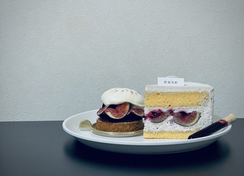 左:ビオレソリエス(黒いちじく)のタルト。円型のタルト生地にカットされたいちじく。もたっと乗った生クリーム。
右:いちじくのショートケーキ。外側はうっすら灰色の生クリーム、スポンジの間に挟んだいちじくの果汁(もしくはカシスソース)が白いクリームに滲み出ている。手前に小さな試験管ケースに入れられた赤ワインとカシスのソース。