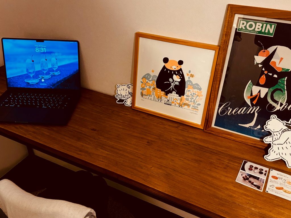 机上の写真。右にシルクスクリーンやポストカード、左にノートパソコン斜め置き（実際は平行に置かないと使いづらいので、これは格好つけ）。